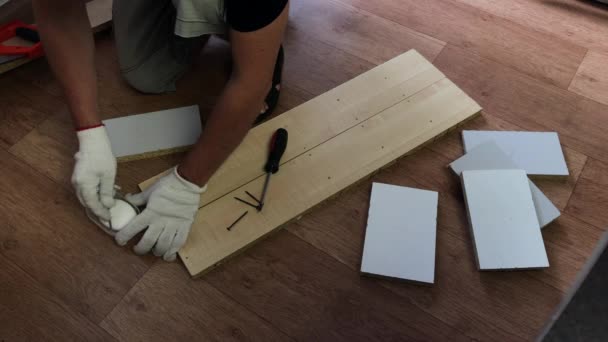 Um homem engraxa um parafuso auto-roscante com sabão e envolve-o em uma placa. Fazendo móveis em casa . — Vídeo de Stock