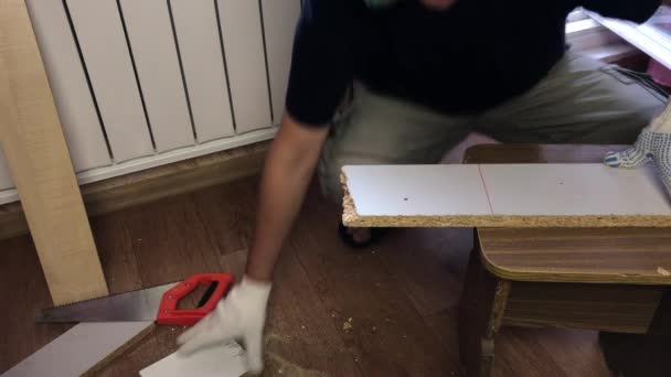 En man klipper en bräda med en bågfil längs en linje. Att göra möbler hemma. — Stockvideo