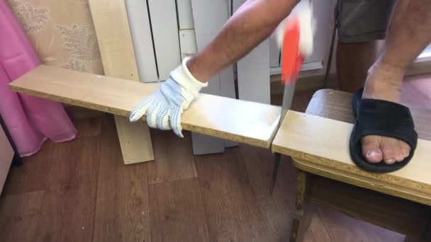 Un hombre está aserrando una tabla con una sierra. Coloca dos tablas iguales verticalmente lado a lado. Hacer muebles en casa. — Vídeos de Stock