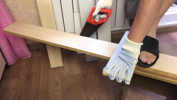 Een man zaagt een plank met een ijzerzaag. meubelen thuis maken. — Stockvideo