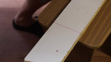 Bir adam rehber boyunca demir testeresiyle tahtayı kesiyor. Kesme çizgisi boyunca.