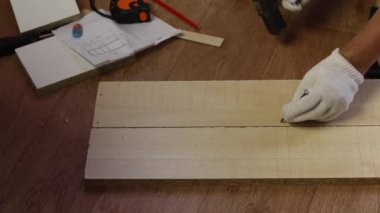 Bir adam bir rafın önünde çömeliyor. Tahtadaki vidalar için yerleri çiviyle işaretliyor. Evde mobilya yapmak.