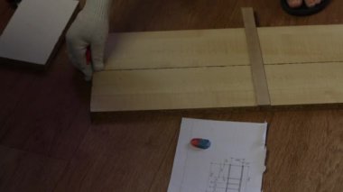 Bir adam bir rafın önünde çömeliyor. Kurusıkı mermiler yakınlarda. Tahtaları kurşun kalemle işaretliyor. Evde mobilya yapmak.