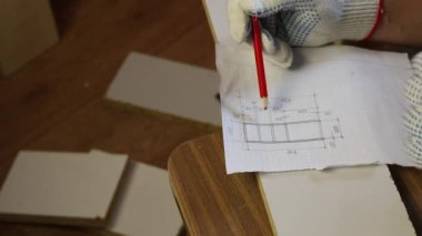 Bir adam tahtadan yapılmış bir rafın çizimini inceliyor. Resmin üzerine bir kalem çizer. Evde mobilya yapmak.