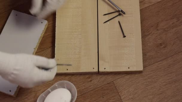 L'homme est accroupi devant les blancs pour l'étagère. Lubrifie la vis autotaraudeuse avec du savon et la visse dans la planche. Fabrication de meubles à la maison. — Video