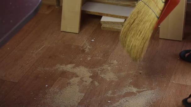 L'homme enlève la sciure de bois du sol. Fabrication de meubles à la maison. — Video