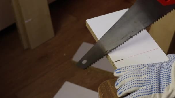 Making furniture at home. A man cuts a board with a hacksaw along the marked line. — Stock Video