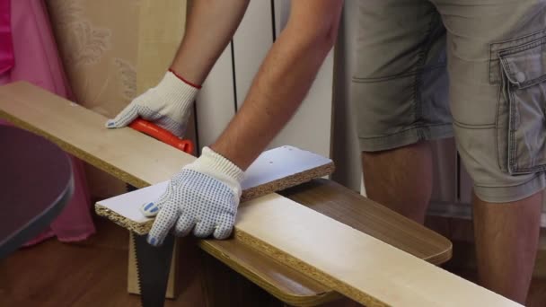 Muž řeže prkno pilou na dřevo. Výroba nábytku doma. — Stock video