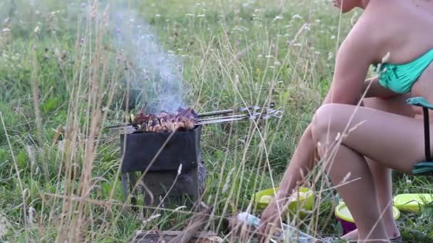 Una donna prepara un barbecue sulla griglia. La carne fritta su spiedi è visibile. La donna regola gli spiedini e spruzza il kebab con acqua. — Video Stock