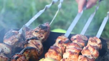 Izgaranın üstünde şiş kebap var. Şiş üzerinde kızarmış et görülebilir. Kadın şişleri ayarlar ve kebabı suyla doldurur..