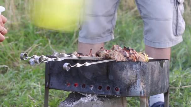 Muž a žena připravují gril na grilu. Smažené maso a zelenina jsou viditelné na špejlích. Ten muž fouká vzduch přes uhlíky. Žena upraví špejle.. — Stock video