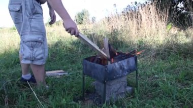 Yanan odunlu metal brazier. Ateş ve duman görünür. Odun onun yanında yatıyor. Yanan odunları düzelten bir adam.