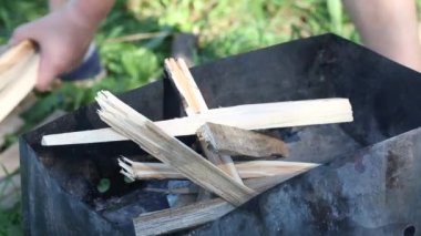 Adam brazier 'a odun koyuyor. Duman görünür. Barbekü çayırdaki çimlerin arasında duruyor. Yakın çekim.