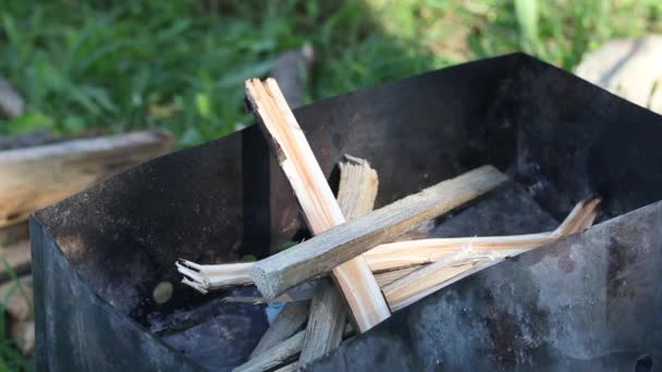 Muž zapálí dřevo a papír v grilu. Grilování stojí mezi trávou na louce. Detailní záběr. — Stock video