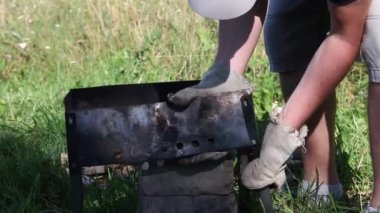 Bir adam metal elementlerden Brezilya biberi toplar. Bağların yan yüzeyleri. Barbekü çayırdaki çimlerin arasında duruyor. Yakın çekim.