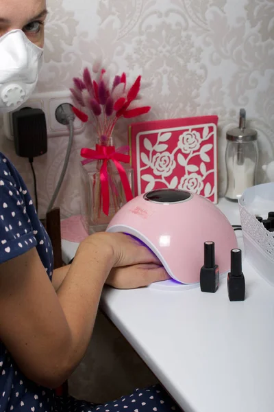 A woman gives herself a manicure. Dries the varnish in a UV lamp. Next to the nail Polish in bottles.