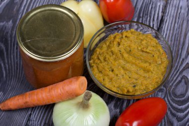 Yeni hazırlanmış kabak havyarı bir kabın içinde. Yanında, kavanozda konserve kabak havyarı. Masanın yüzeyinde sebzeler, yemek pişirmek için malzemeler..