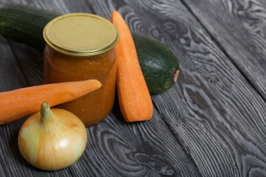 Kavanozda konserve kabak havyarı. Masanın yüzeyinde sebzeler, yemek pişirmek için malzemeler var..