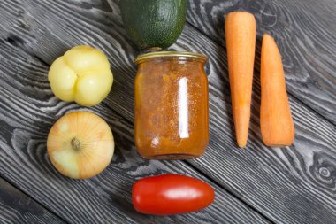 Kavanozda konserve kabak havyarı. Masanın yüzeyinde sebzeler, yemek pişirmek için malzemeler var..
