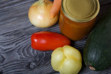 Kavanozda konserve kabak havyarı. Masanın yüzeyinde sebzeler, yemek pişirmek için malzemeler var..