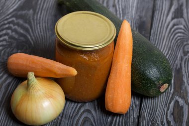 Kavanozda konserve kabak havyarı. Masanın yüzeyinde sebzeler, yemek pişirmek için malzemeler var..