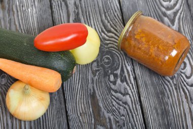 Kavanozda konserve kabak havyarı. Masanın yüzeyinde sebzeler, yemek pişirmek için malzemeler var..