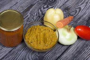 Yeni hazırlanmış kabak havyarı bir kabın içinde. Yanında, kavanozda konserve kabak havyarı. Masanın yüzeyinde sebzeler, yemek pişirmek için malzemeler..