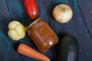 Kavanozda konserve kabak havyarı. Masanın yüzeyinde sebzeler, yemek pişirmek için malzemeler var..