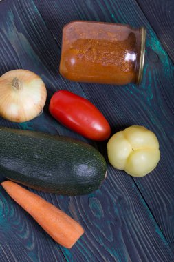Kavanozda konserve kabak havyarı. Masanın yüzeyinde sebzeler, yemek pişirmek için malzemeler var..