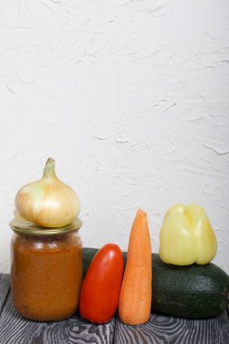 Kavanozda konserve kabak havyarı. Masanın yüzeyinde sebzeler, yemek pişirmek için malzemeler var..