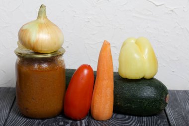 Kavanozda konserve kabak havyarı. Masanın yüzeyinde sebzeler, yemek pişirmek için malzemeler var..