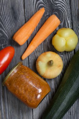 Kavanozda konserve kabak havyarı. Masanın yüzeyinde sebzeler, yemek pişirmek için malzemeler var..