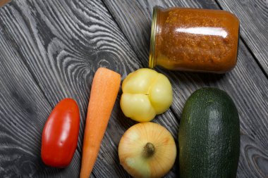 Kavanozda konserve kabak havyarı. Masanın yüzeyinde sebzeler, yemek pişirmek için malzemeler var..