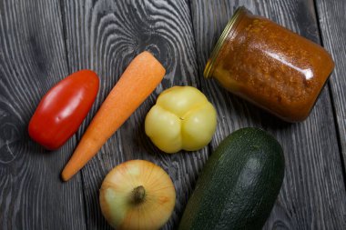 Kavanozda konserve kabak havyarı. Masanın yüzeyinde sebzeler, yemek pişirmek için malzemeler var..