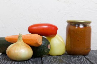 Kavanozda konserve kabak havyarı. Masanın yüzeyinde sebzeler, yemek pişirmek için malzemeler var..