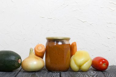 Kavanozda konserve kabak havyarı. Masanın yüzeyinde sebzeler, yemek pişirmek için malzemeler var..