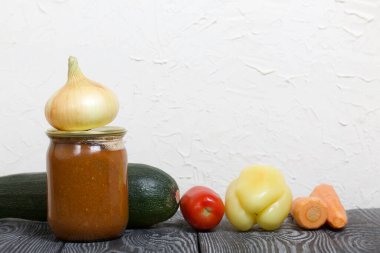 Kavanozda konserve kabak havyarı. Masanın yüzeyinde sebzeler, yemek pişirmek için malzemeler var..