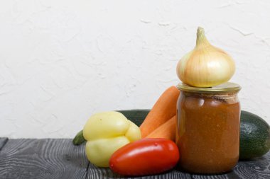 Kavanozda konserve kabak havyarı. Masanın yüzeyinde sebzeler, yemek pişirmek için malzemeler var..