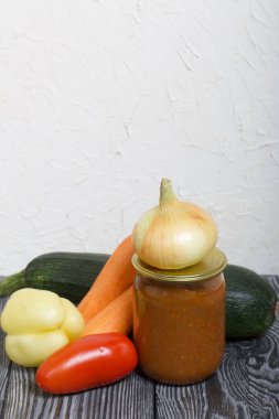 Kavanozda konserve kabak havyarı. Masanın yüzeyinde sebzeler, yemek pişirmek için malzemeler var..