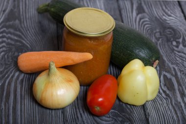 Kavanozda konserve kabak havyarı. Masanın yüzeyinde sebzeler, yemek pişirmek için malzemeler var..