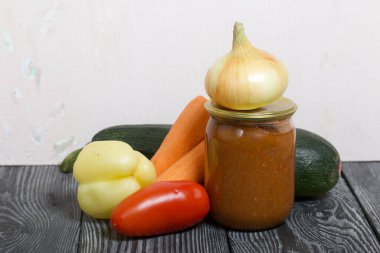 Kavanozda konserve kabak havyarı. Masanın yüzeyinde sebzeler, yemek pişirmek için malzemeler var..