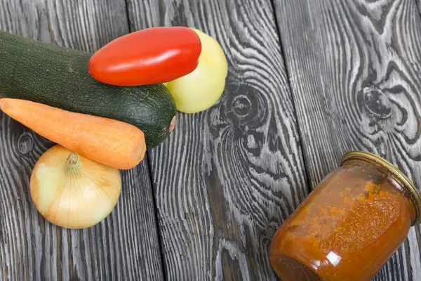 Kavanozda konserve kabak havyarı. Masanın yüzeyinde sebzeler, yemek pişirmek için malzemeler var..