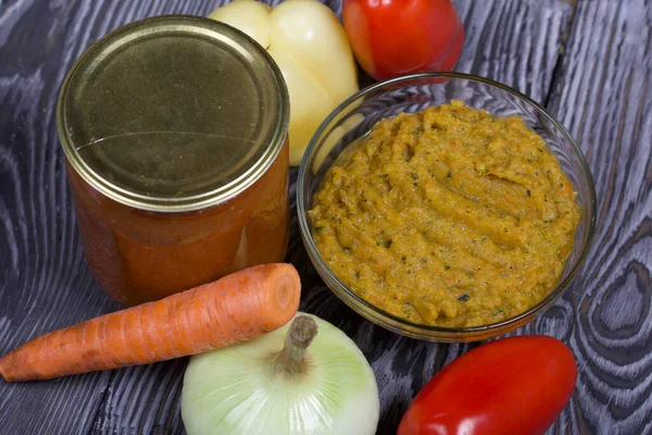 Yeni hazırlanmış kabak havyarı bir kabın içinde. Yanında, kavanozda konserve kabak havyarı. Masanın yüzeyinde sebzeler, yemek pişirmek için malzemeler..