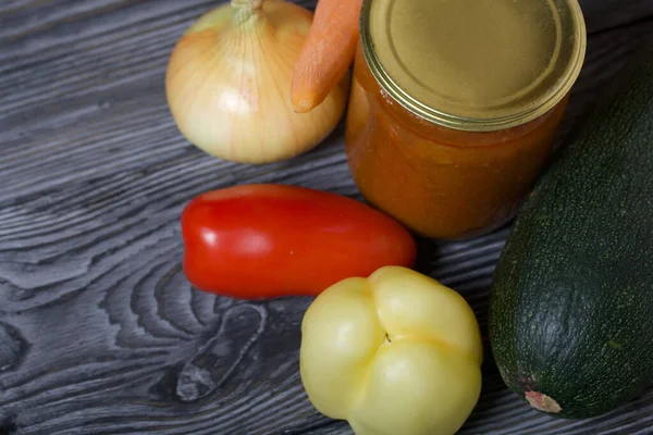 Kavanozda konserve kabak havyarı. Masanın yüzeyinde sebzeler, yemek pişirmek için malzemeler var..