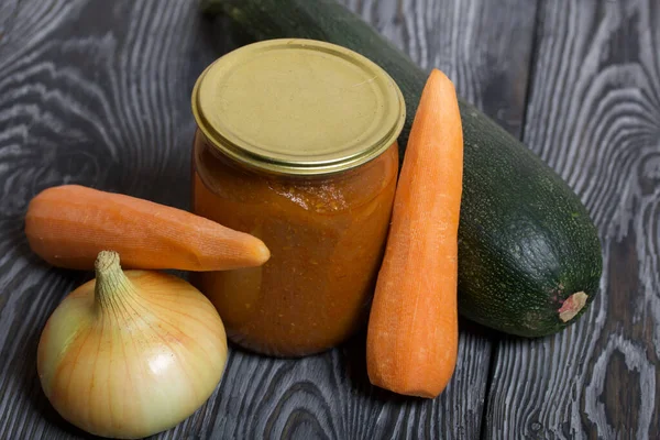 Kavanozda konserve kabak havyarı. Masanın yüzeyinde sebzeler, yemek pişirmek için malzemeler var..