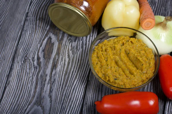 Yeni hazırlanmış kabak havyarı bir kabın içinde. Yanında, kavanozda konserve kabak havyarı. Masanın yüzeyinde sebzeler, yemek pişirmek için malzemeler..