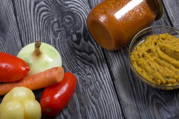 Yeni hazırlanmış kabak havyarı bir kabın içinde. Yanında, kavanozda konserve kabak havyarı. Masanın yüzeyinde sebzeler, yemek pişirmek için malzemeler..