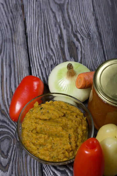 Yeni hazırlanmış kabak havyarı bir kabın içinde. Yanında, kavanozda konserve kabak havyarı. Masanın yüzeyinde sebzeler, yemek pişirmek için malzemeler..