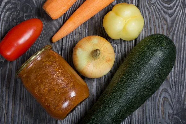 Kavanozda konserve kabak havyarı. Masanın yüzeyinde sebzeler, yemek pişirmek için malzemeler var..