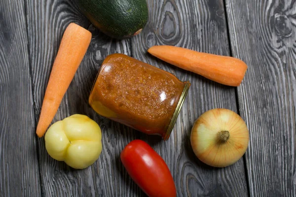 Kavanozda konserve kabak havyarı. Masanın yüzeyinde sebzeler, yemek pişirmek için malzemeler var..